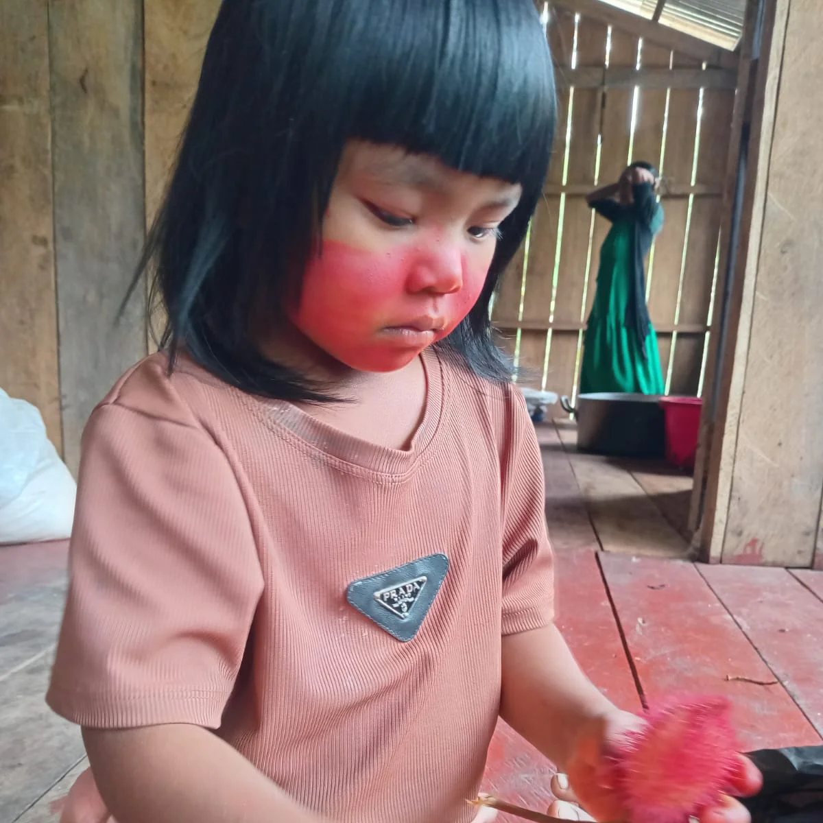 Child with red face paint looking at a red object indoors
